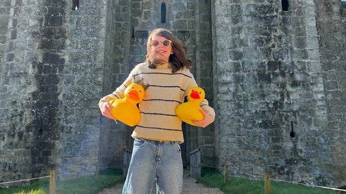 A person holding a giant rubber yellow duck outside the castle gate.